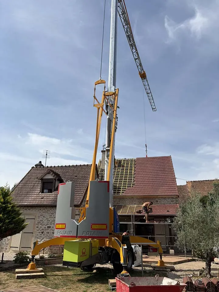 Grue devant une maison avec une toiture en réfection et benne rouge