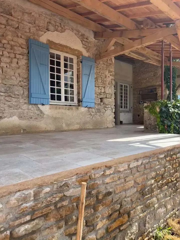 Terrasse rénovée d'une batisse en pierre et volets bleus